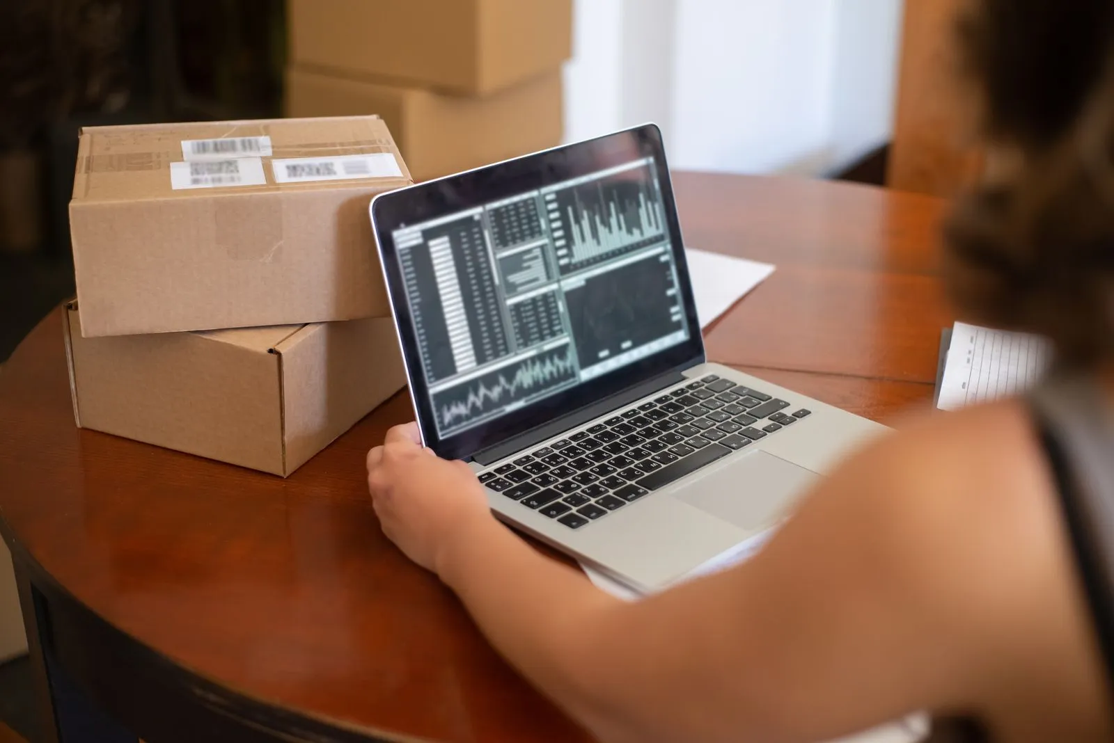 A small business owner checking sales charts on a laptop next to shipping boxes