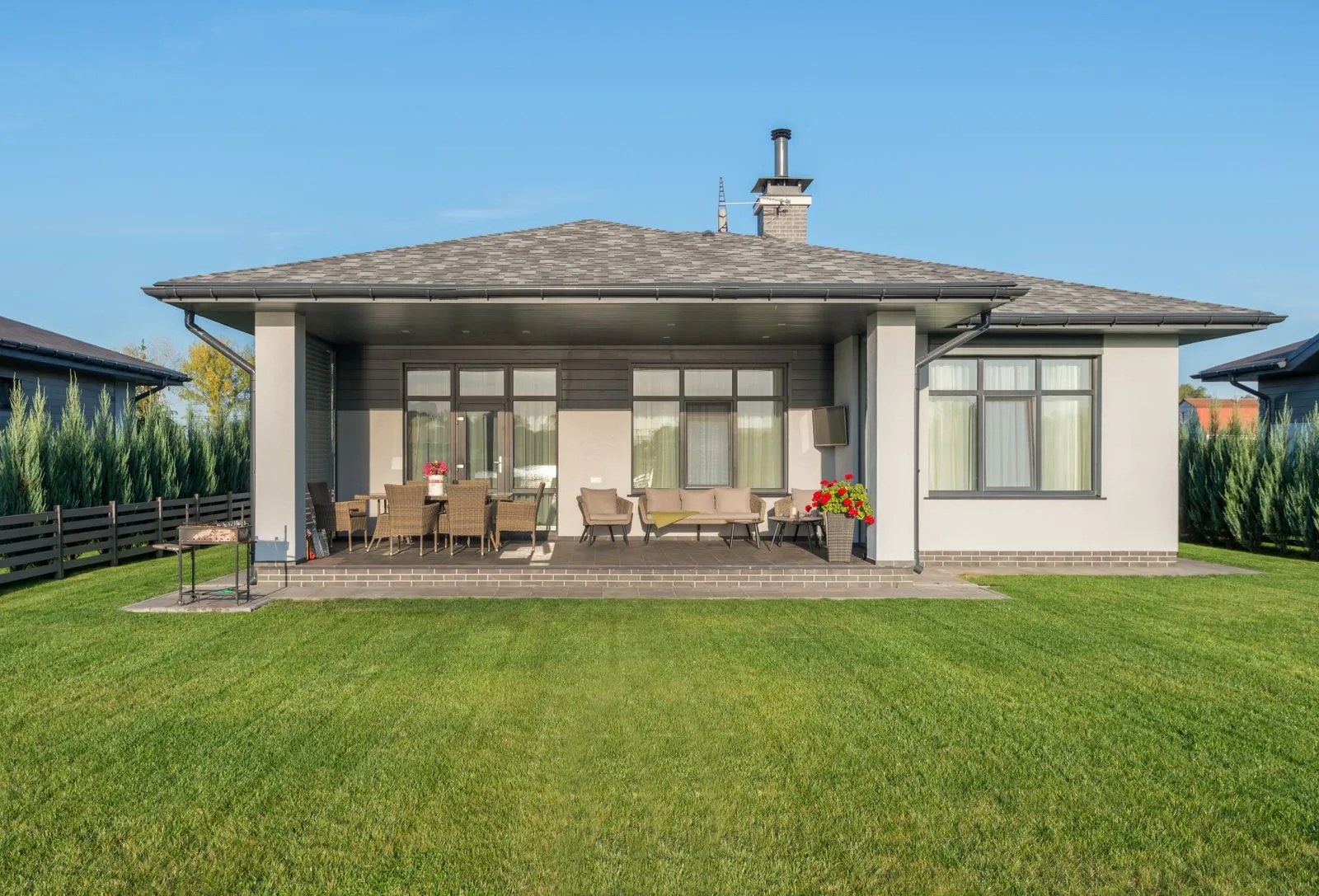 A covered patio with outdoor seating facing a wide lawn