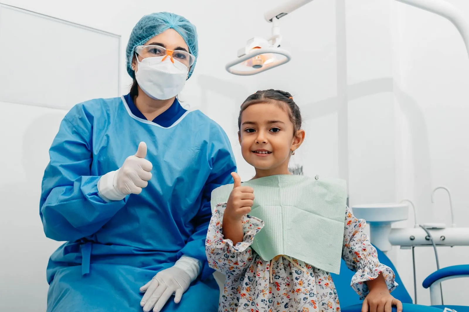 A dentist and a smiling young girl giving a thumbs up in the dental chair