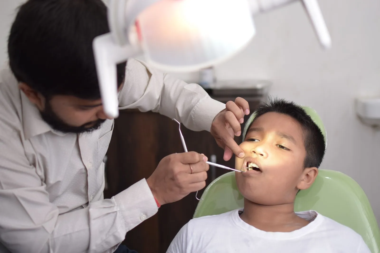 A dentist checking a boy’s teeth with a small mirror