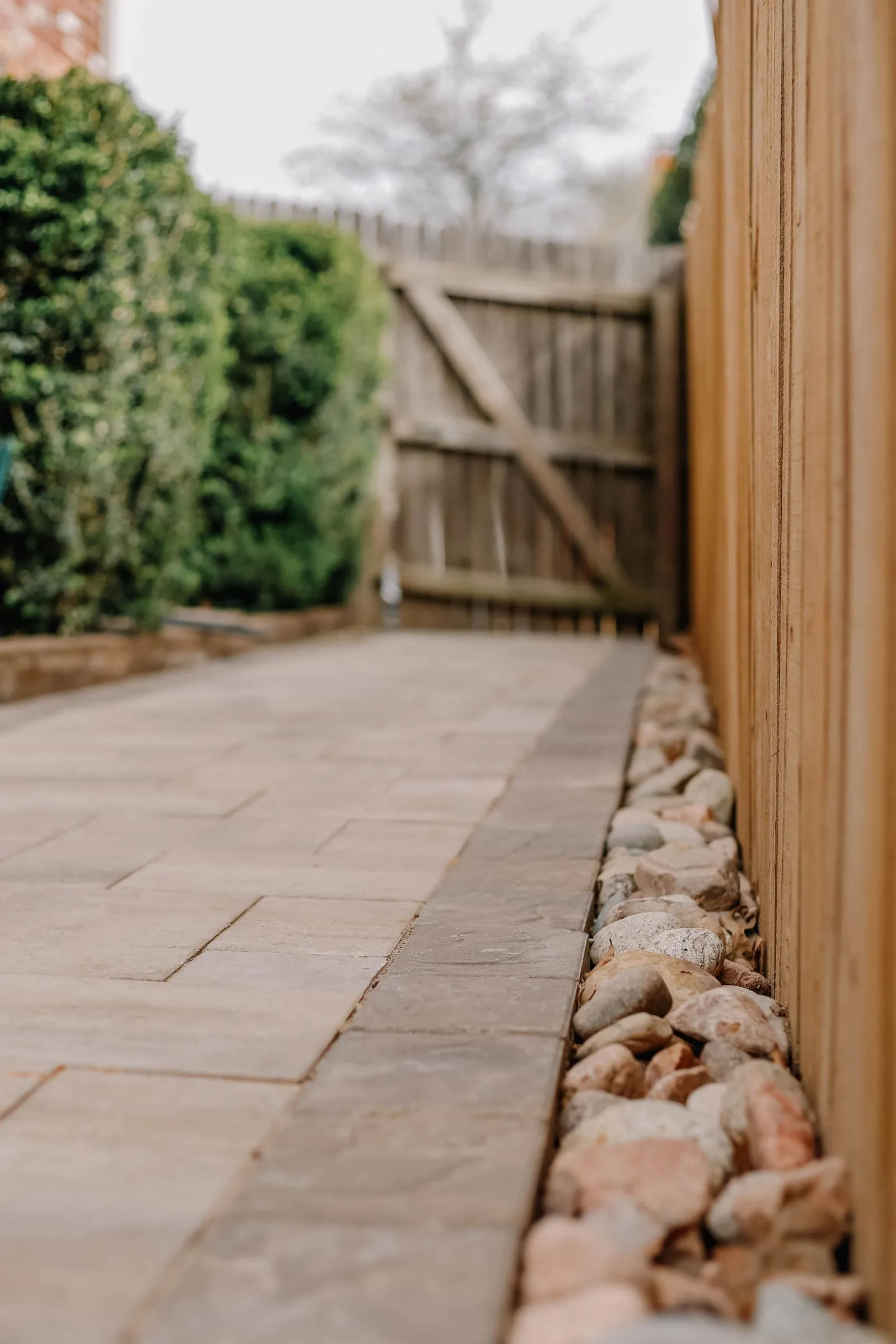 A stone paver side yard with river rock along a wood fence