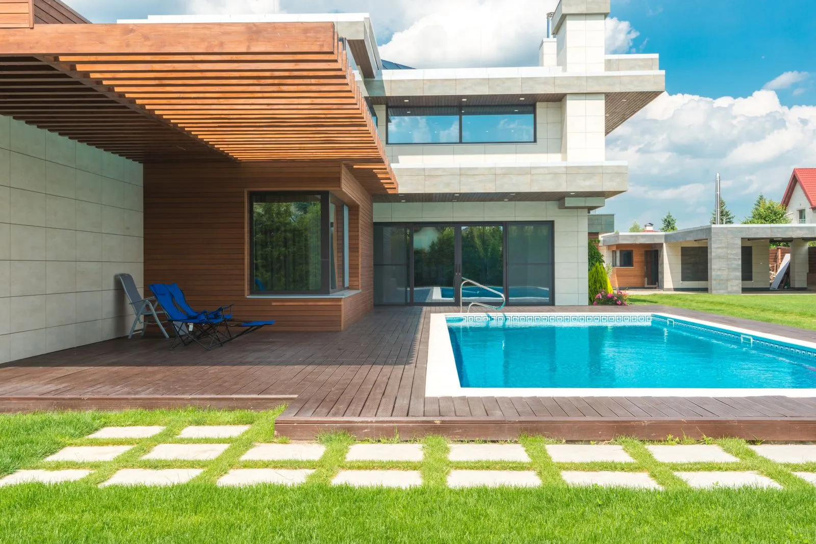 A pool and wood deck with stepping stones across the lawn